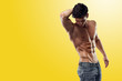 © Dragosh - A strong athletic brunette young man model showing six pack abs and holding his hand behind head, looking down, isolated on yellow background. Copy space. Horizontal studio shot.
