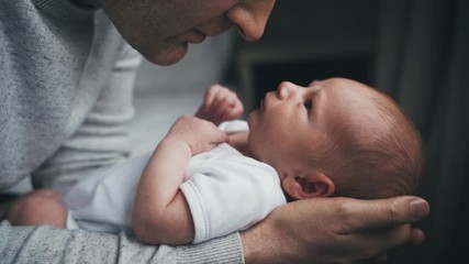 dad in grey sweater kisses his newborn baby on the nose. tiny baby in white outfit rests in the arms