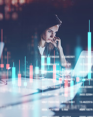 Young woman working at night modern office loft.Red and green candlestick chart and stock trading on background. Double exposure