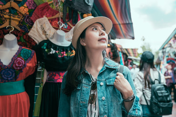 Wall Mural - beautiful happy curious young asian woman traveler walking through Olvera Street in los angeles. female tourist looking and choosing clothes gifts in mexico markets. Shopping and vacation theme.