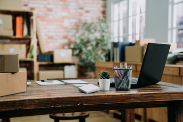 Trendy modern open concept loft office space with windows natural light. wood workplace table with laptop computer in warehouse company. start up small online business studio indoors interior.