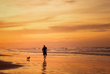 Silhouette Of Man Running With Dog In The Beach In Sunset Time