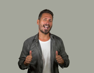 Wall Mural - young happy and handsome 40s man with blue eyes and beard  in casual shirt posing in cool attitude smiling cheerful and confident on grey background gesturing positive