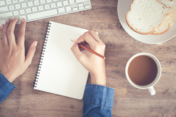 Wall Mural - top view of woman business hand writing on the notebook and using computer on desk and have coffee, 