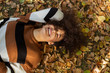 © therabbithole - Young afro american woman lying on autumnal leaves in sunny park.