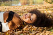 © therabbithole - Young afro american woman lying on autumnal leaves in sunny park.