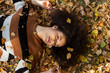 © therabbithole - Young afro american woman lying on autumnal leaves in sunny park.