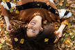 © therabbithole - Young afro american woman lying on autumnal leaves in sunny park.