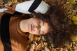 © therabbithole - Young afro american woman lying on autumnal leaves in sunny park.