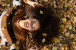 © therabbithole - Young afro american woman lying on autumnal leaves in sunny park.