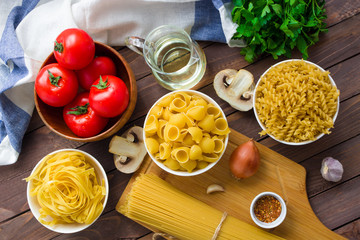 ingredients for cooking italian pasta raw spaghetti fusilli tagliatelle fresh tomatoes mushrooms onion parsley garlic olive oil on rustic wooden background top view