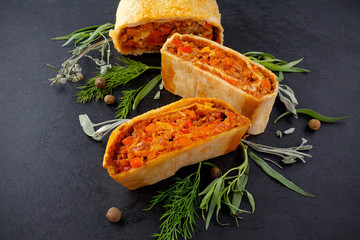 strudel with meat and mushrooms on a black board with fresh leaves