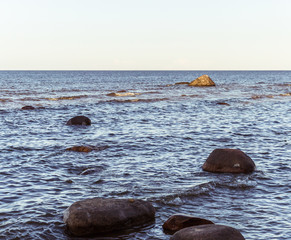 The Baltic Sea with big stones in the water, the water is calm with small waves, the horizon and the light sky are visible