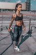 © byswat - Girl athlete in tattoos, in summer in city, trains fitness, gymnastics workout. Sportswear leggings top. In the morning before the run. Background steps. It warms the muscles before exercise.