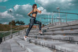 © byswat - Girl runs in the summer in the city, on morning run. Stair background, blue sky with clouds. Clothing leggings top. Free space for text. Phone earphones.