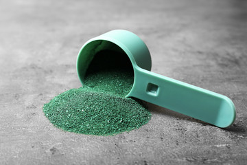 Scoop and spirulina algae powder on grey background