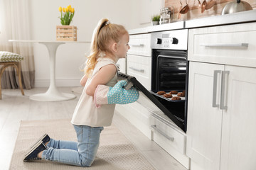 Wall Mural - Little girl opening door of oven with cookies in kitchen