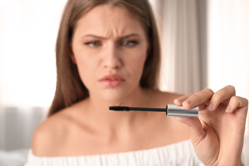 Poster - Emotional young woman holding mascara brush with fallen eyelashes indoors, closeup