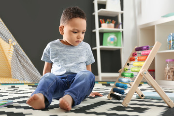 Wall Mural - Cute little African-American child playing with abacus on floor in kindergarten. Indoor activity