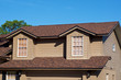 © Stephen Orsillo - View of generic brown two story American house against blue sky with gables windows.