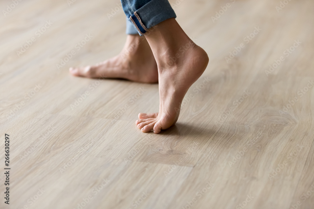 Side closeup view woman feet stands on warm wooden floor - obrazy, fototapety, plakaty 