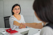 © mrwinn - Smiling Asian woman shaking hand while sitting at her desk in an office or business environment.