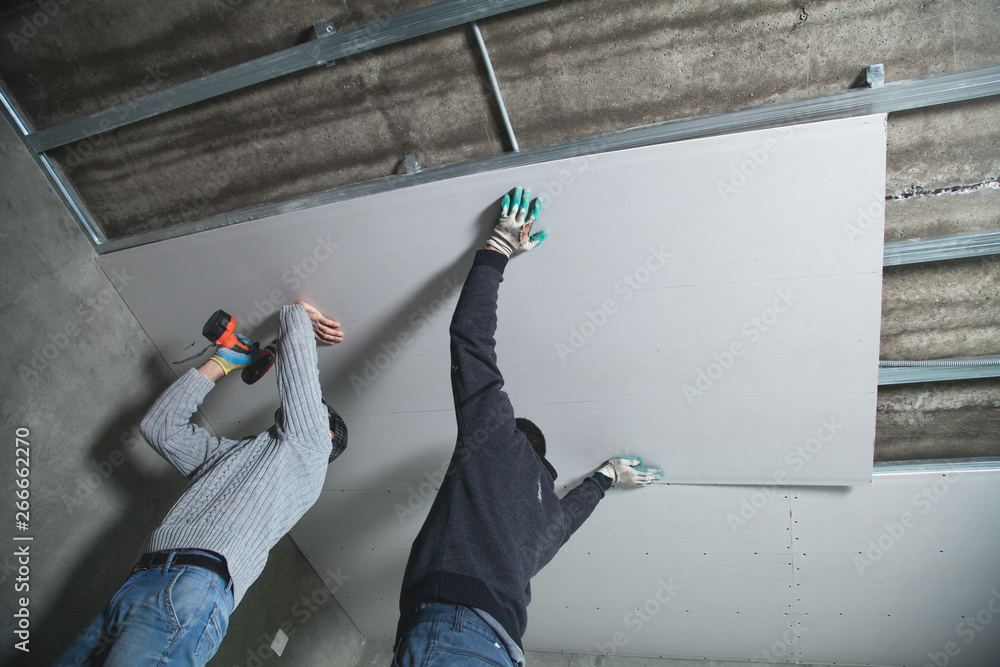 Workers fitting panel into frame of ceiling. - obrazy, fototapety, plakaty 