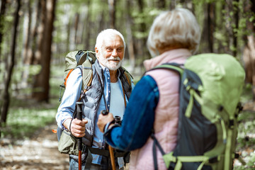 Wall Mural - Beautiful senior couple hiking with backpacks and trekking sticks in the forest. Concept of active lifestyle on retirement