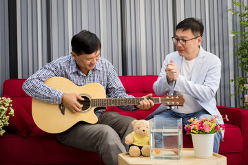 two people retirement seniors sitting on a sofa playing guitar happily in the living room.