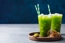 Matcha Ice Tea In Tall Glass On Wooden Plate. Blue Background. Copy Space.