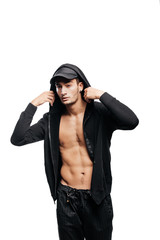 Wall Mural - Handsome young dancer dressed in a sweatshirt on a naked torso with a hood on the cap  and black pants stands with his hands on the  hood