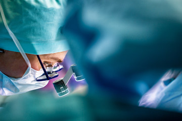 Wall Mural - Surgeon performing surgery in hospital operating room. Surgeon in mask wearing loupes during medical procadure.