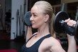 © viktoriya - girls blonde with long hair in a black sports top and black leggings doing sports exercises dumbbells in the gym