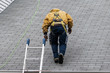 © Andriy Blokhin - House during day with gray color Single Family Home and construction man in yellow uniform walking on roof shingles and ladder during repair