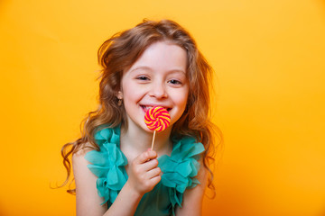 Beautiful little girl with sugar lollipop on yellow background