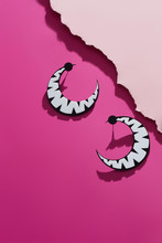 A Shot Of Massive Earrings In The View Of A Cheshire Cat's Smile. The Trendy Set Is Isolated Asymmetrically Against The Pink Background, Near Pale Pink Ragged Platform. Voguish Women's Fashion Item.