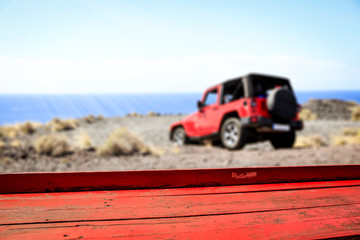 Red old wooden table. A summer car on the cliffs of Gran Canaria island. A place for your products. Summer time and ocean landscape