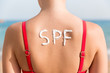 © sosiukin - SPF word made of sunblock at woman's back at the beach. Sun protection factor concept