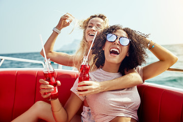 Wall Mural - Laughing friends sitting on a boat having drinks during vacation