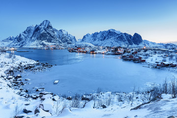 Wall Mural - Scenic view of historic village Reine on Lofoten Islands archipelago in Norway, Scandinavia. Picturesque twilight landscape of northern nature. Sophisticated snow-capped rocks in background.