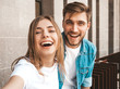 © halayalex - Smiling beautiful girl and her handsome boyfriend in casual summer clothes. Happy family taking selfie self portrait of themselves on smartphone camera. Having fun on the street background