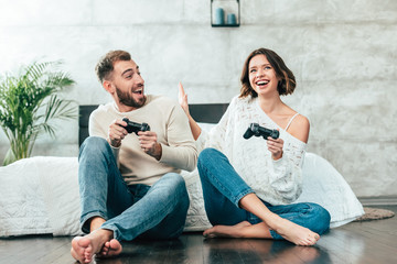 surprised man looking at cheerful woman playing video game at home