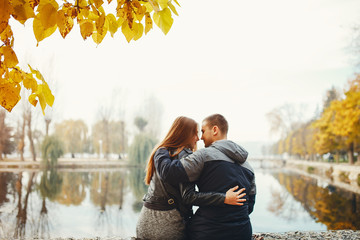 Cute couple sitting in a autumn park. Boy and girl have fun near river