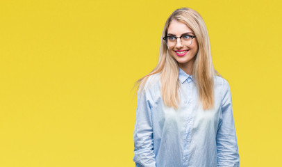 Poster - Young beautiful blonde business woman wearing glasses over isolated background looking away to side with smile on face, natural expression. Laughing confident.