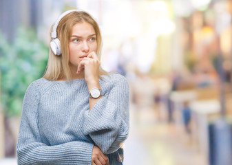 Poster - Young caucasian woman listening to music wearing headphones over isolated background looking stressed and nervous with hands on mouth biting nails. Anxiety problem.