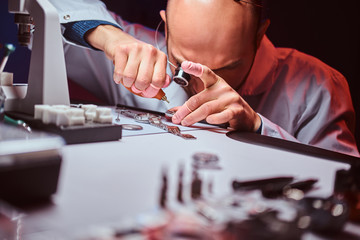 Expirienced watchmaker is doing engraving for custmer's watch at his workshop.