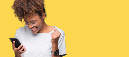 Wall Mural - Young african american woman using smartphone over isolated background screaming proud and celebrating victory and success very excited, cheering emotion