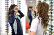 © Alexey - young pretty woman is trying sun glasses on at an eyewear shop with help of a shop assistant, low depth of field