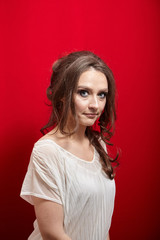 Wall Mural - Portrait of young woman on red background. Attractive lady with long wavy brown hair in white blouse