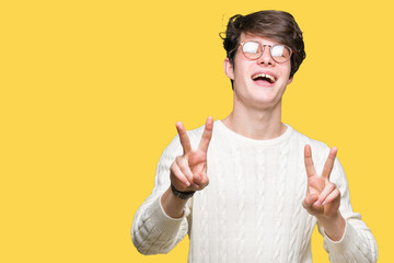 Young handsome man wearing glasses over isolated background smiling looking to the camera showing fingers doing victory sign. Number two.